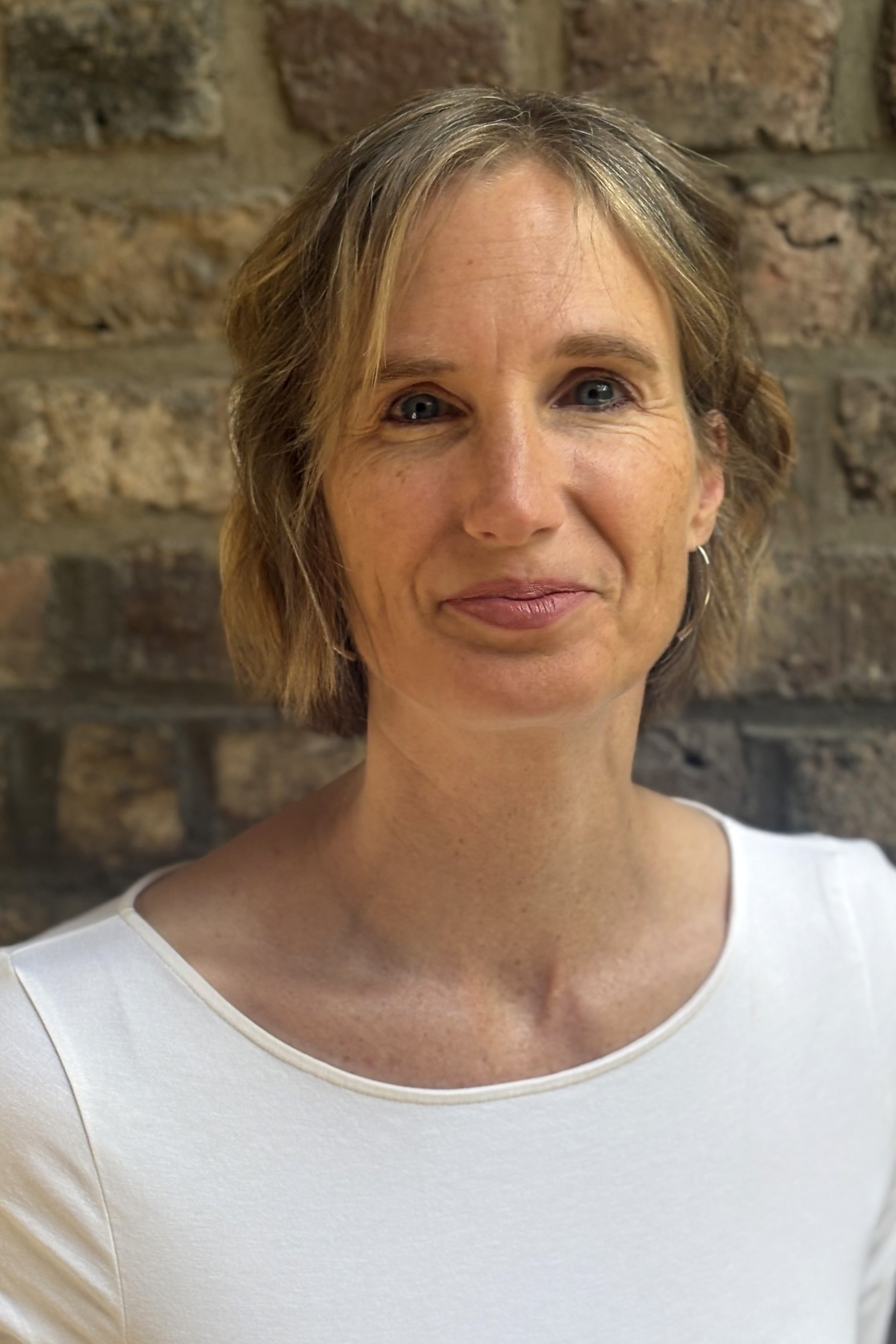 Portrait photo of a blond woman in a white shirt standing in front of a brick wall